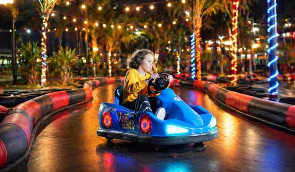 Child driving a bumper kart on a lit outdoor event track